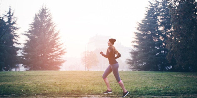 Young woman jogging outside in sunny autumn forest. The sun is shining in the background .