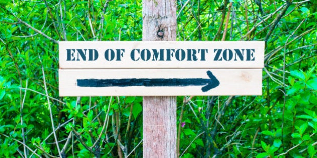 END OF COMFORT ZONE written on Directional wooden sign with arrow pointing to the right against green leaves background. Concept image with available copy space