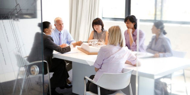 Group of architects and their client discussing model of a new house around a conference room table in a modern architects office.