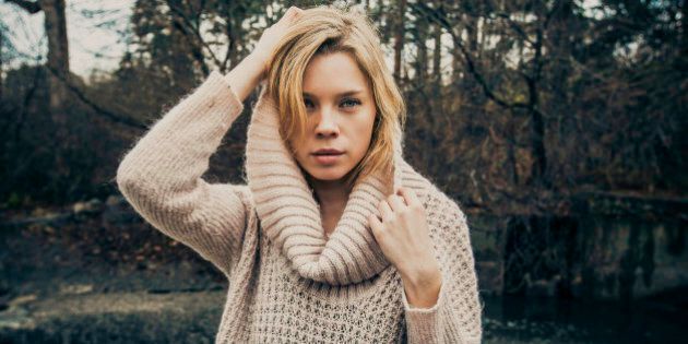 Beautiful blonde model with a large, ribbed-neck sweater by the river.