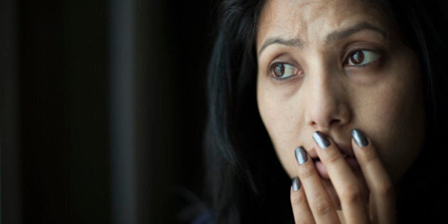 Indoor low key image of a worried and surprised Asian young woman putting her hand on her mouth and looking away at something with frowning gesture. One person, horizontal, head and shoulders composition with copy space and selective focus.