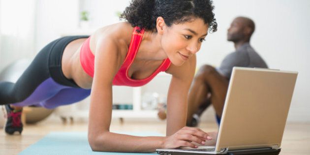 Woman using computer and doing push-ups in gym