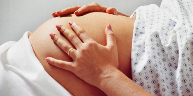 Pregnant woman in hospital gown rubs belly