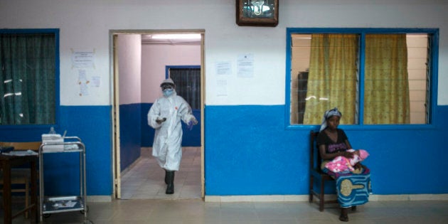 A health worker walks past a woman holding a baby at the maternity ward in the government hospital in Koidu, Kono district, in eastern Sierra Leone, December 20, 2014. Health workers at the hospital are in full protective gear as part of increased precautions since the outbreak of Ebola in West Africa. Sierra Leone, neighbouring Guinea and Liberia are at the heart of the world's worst recorded outbreak of Ebola. Rates of infection are rising fastest in Sierra Leone, which now accounts for more than half of the 18,603 confirmed cases of the virus. REUTERS/Baz Ratner (SIERRA LEONE - Tags: HEALTH DISASTER)