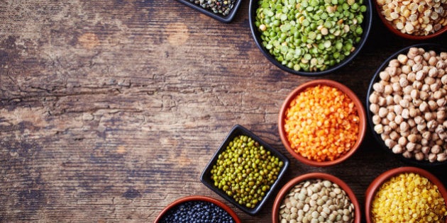 Bowls of various legumes (chickpeas, green peas, red lentils, canadian lentils, indian lentils, black lentils, green lentils; yellow peas, green mung beans) on wooden background