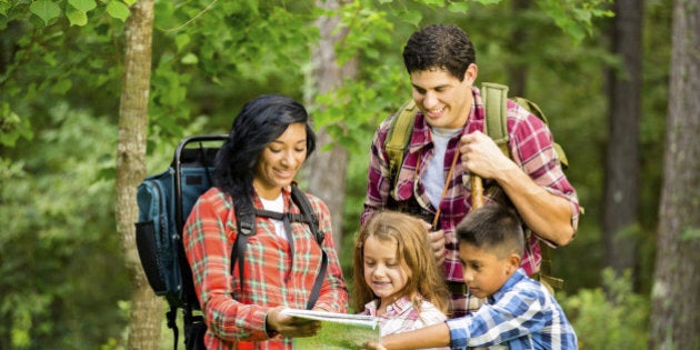 Family of four on vacation. Hiking in a national park. Southern USA. Autumn season. Hispanic and African descent family members. Family pauses to check the map.