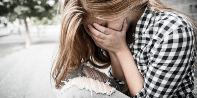 Unhappy depressed teenager with face in hands sitting outdoor