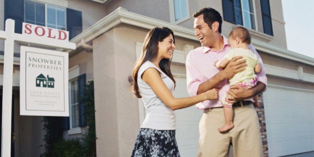 Family with baby girl (12-15 months) standing in front of new house