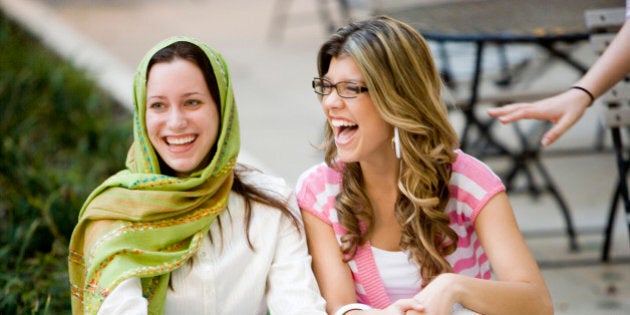 View of two cheerful friends sitting on a curb outside a building