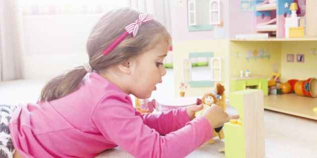 Young girl plays with dolls in dolls house.