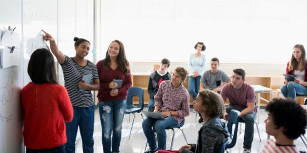 High school students giving presentation whiteboard in classroom