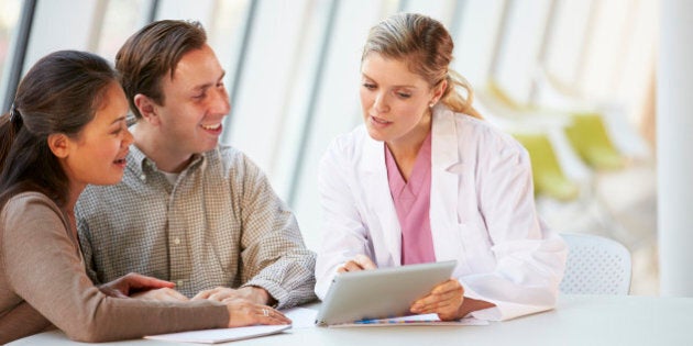 Female Doctor Using Digital Tablet Talking With Patients