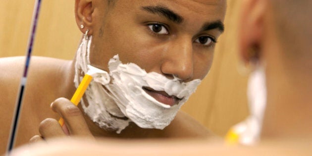 An over the shoulder headshot of an African-American young adult male's reflection in a mirror, he is shaving