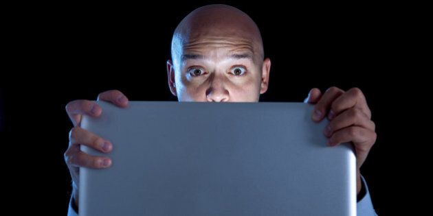 excited businessman alone at night sitting at computer laptop watching porn or online gambling isolated on black background on internet addiction concept