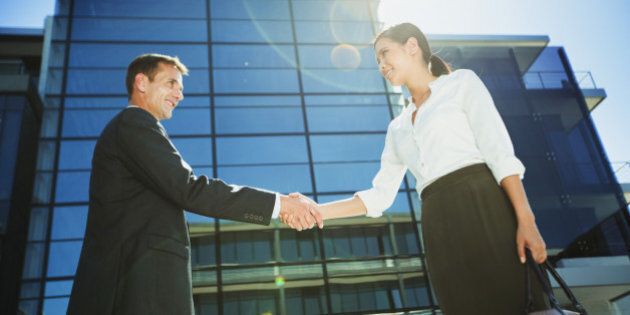 Businessman and businesswoman shaking hands below highrise