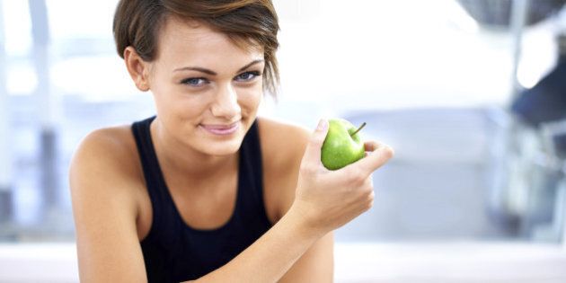 Shot of a sporty young woman sitting on a gym floor eating an apple