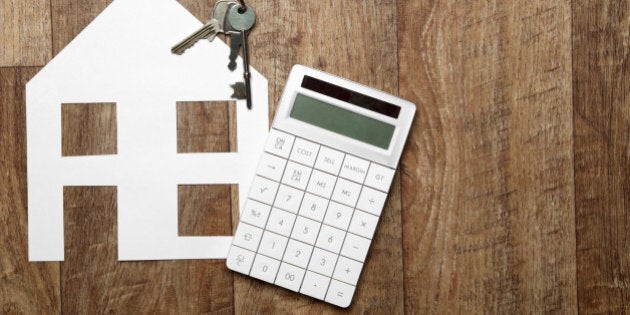 Cutout paper house on a wooden background with keys and calculator