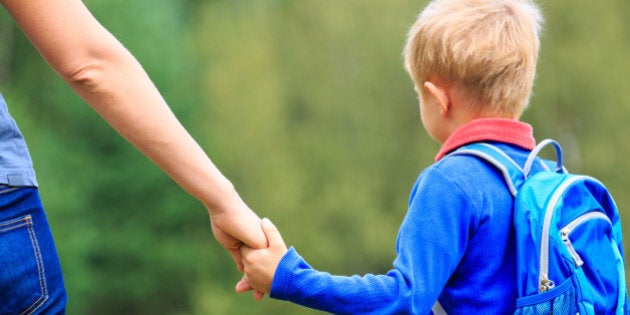 Mother holding hand of little son with backpack outdoors, back to school