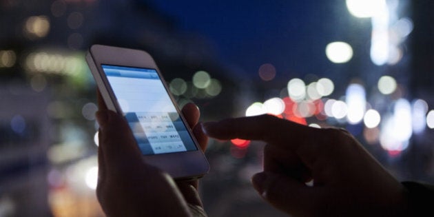 The hands of a woman holding a smart phone and e-mailing on the street at night.