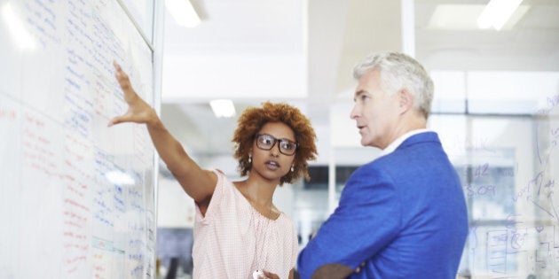 Young businesswoman explaining strategy on whiteboard to male colleague in creative workspace