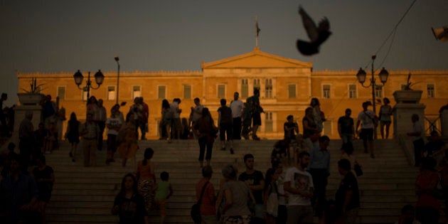 People walk in front of the Greek Parliament in central Athens, Tuesday, July 14, 2015. The eurozone's top official says it's not easy to find a way to get Greece a short-term cash infusion that will help it meet upcoming debt repayments. (AP Photo/Emilio Morenatti)