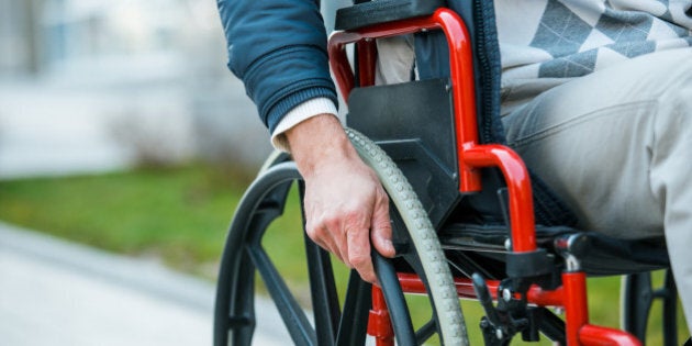 Adult man in wheelchair. Close up photo of male hand on wheel of wheelchair during walk