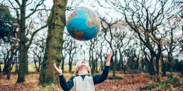 Little boy outdoors in the woods throwing a globe up in the air