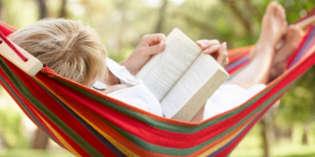 Senior Woman Relaxing In Hammock With Book