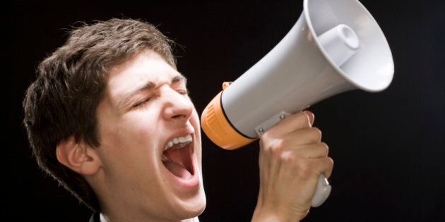 A man is screaming into a loudspeaker against a black background.
