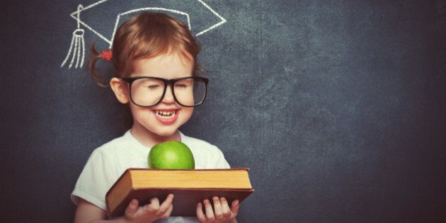 pretty little girl schoolgirl with books and apple in a school board