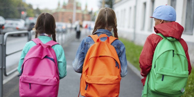 Backs of schoolkids with colorful rucksacks moving in the street