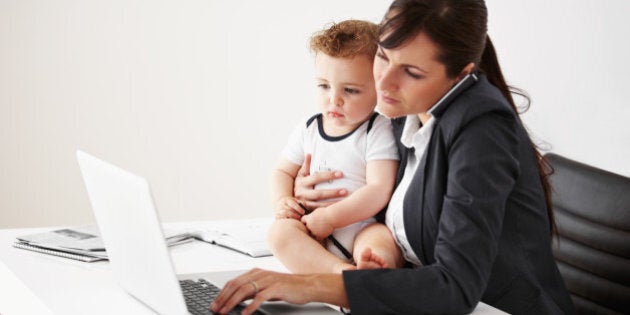 Working mom talking on the phone while holding a baby and typing on her laptop