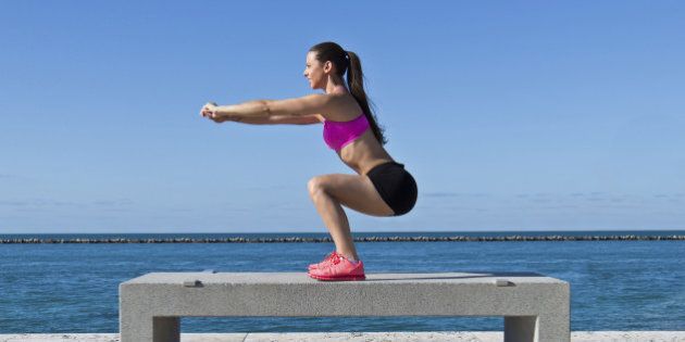 Hispanic woman doing squats on a bench by the ocean