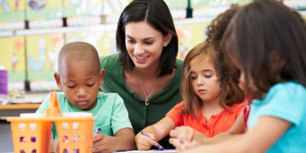 Group Of Elementary Age Children In Art Class With Teacher Sitting Down At Table Drawing