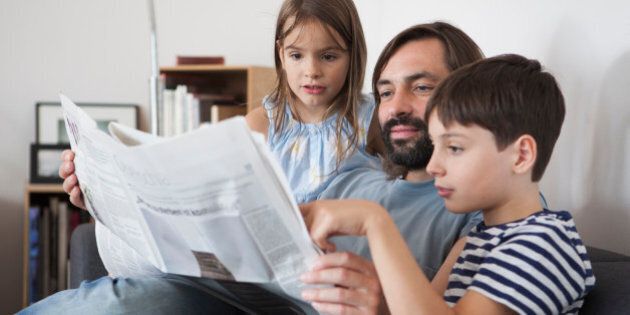 Father and children reading newspaper on sofa at home