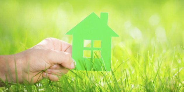 Paper house in children`s hand against green spring background. Real estate concept