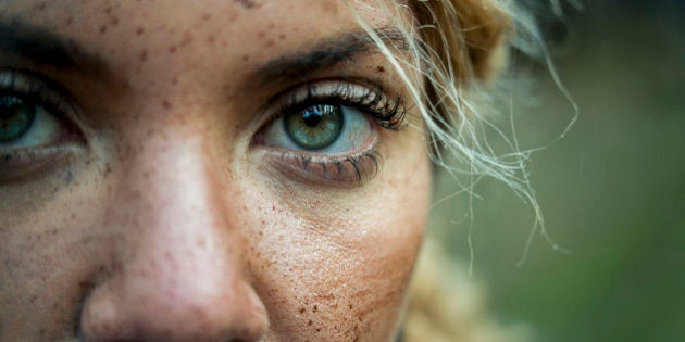 Portrait of a muddy female mountain biker in nature, travel and sports imagery, eyes only, close up looking at camera, landscape composition, one female only aged 25 to 30.