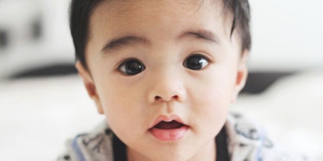 Closeup photo of five month old baby boy (Asian/Filipino) on his tummy staring at the camera. He has a heart shaped mouth.