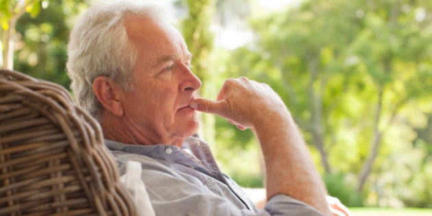 Pensive senior man sitting in wicker armchair on porch