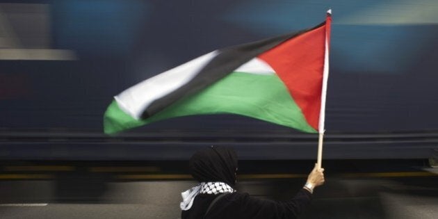 A woman holds a Palestinian flag as a truck passes by, during a protest against Grammy-winning American musician Pharrell Williams near the Grand west Casino where he was holding a concert in Cape Town, on 21 September, 2015. Supporters of the Boycott, Divestment and Sanctions (BDS) campaign were protesting against the singer's partnership with major South African retail group Woolworths, over its imports from Israel. BDS accuses Woolworths of importing Israeli agricultural produce grown in the occupied Palestinian territories, a charge the company denies. AFP PHOTO / RODGER BOSCH (Photo credit should read RODGER BOSCH/AFP/Getty Images)