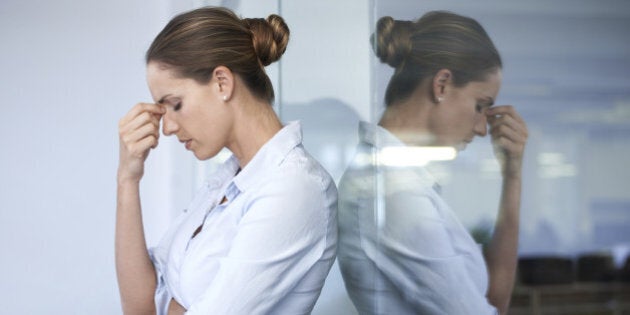 A young businesswoman standing against a glass wall with her head in her hand