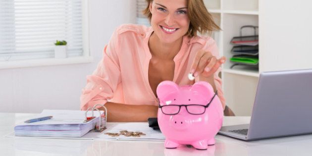 Happy Woman With Bills Putting Coin In Piggybank At Desk