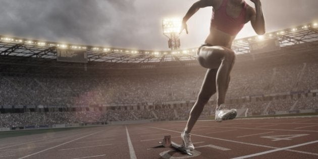 female athlete bursting out of blocks on athletics track in full floodlit stadium under dramatic sky