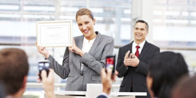 Attractive businesswoman receives applause on stage while holding up an award. Horizontal shot.