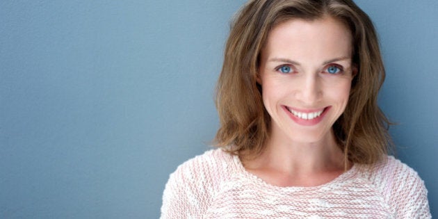 Close up portrait of a beautiful older woman smiling with sweater on blue background