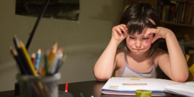 little girl at the table looking a little frustrated at her exercise book.