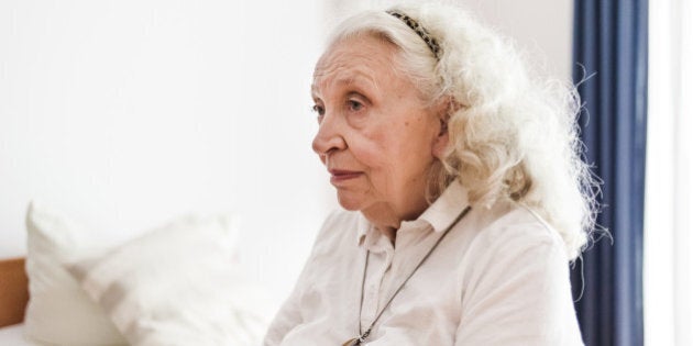 Lonesome senior woman sitting at her bed in retirement home.