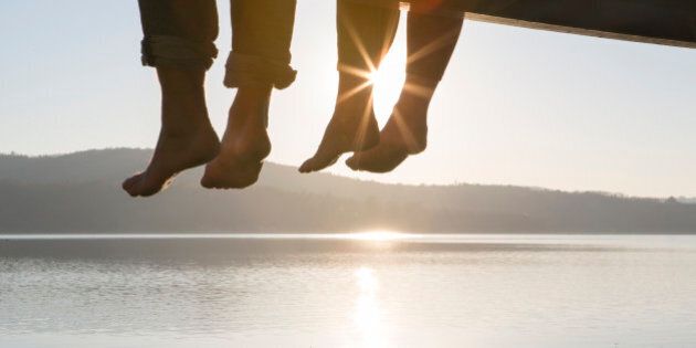 Couple's feet dangle from dock,above tranquil lake