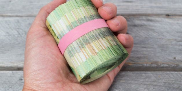 Hand holding a roll of green bank notes against wooden table