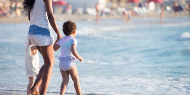 Rear view of 2 and 3 years multiracial little girls playing together with their mother at the beach.